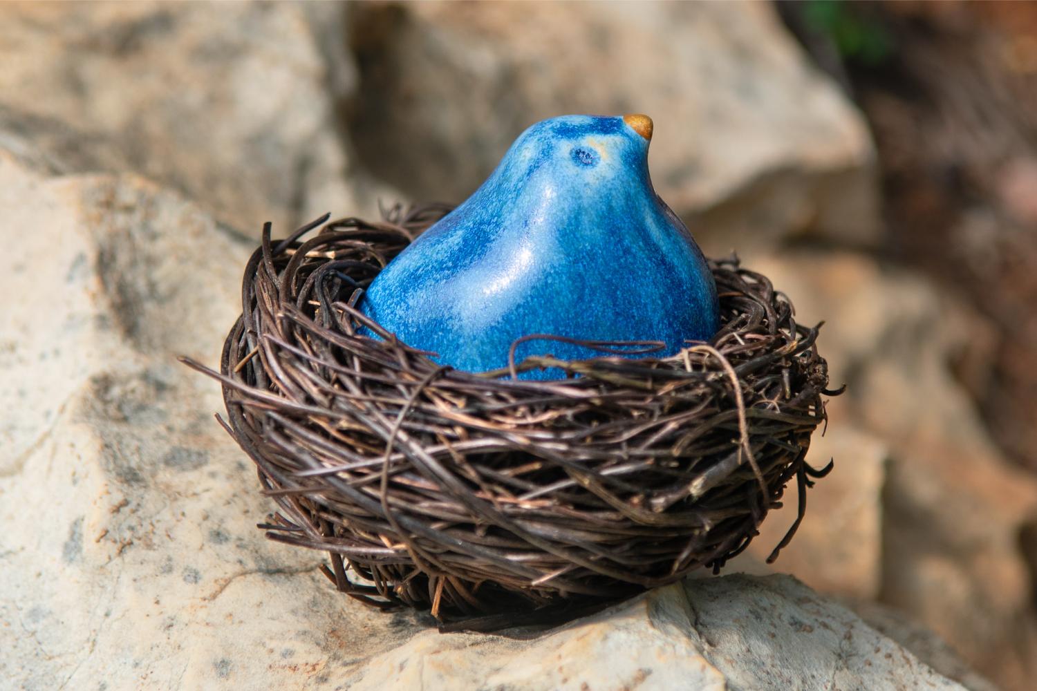 Glazed blue stoneware bird in a natural fiber nest